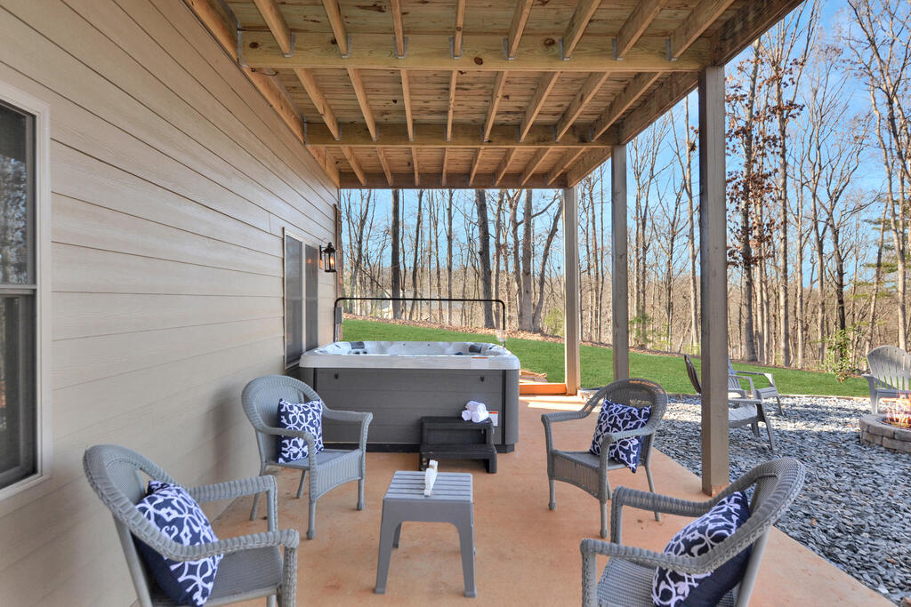 Covered patio with a hot tub and wicker seating overlooking a wooded yard.