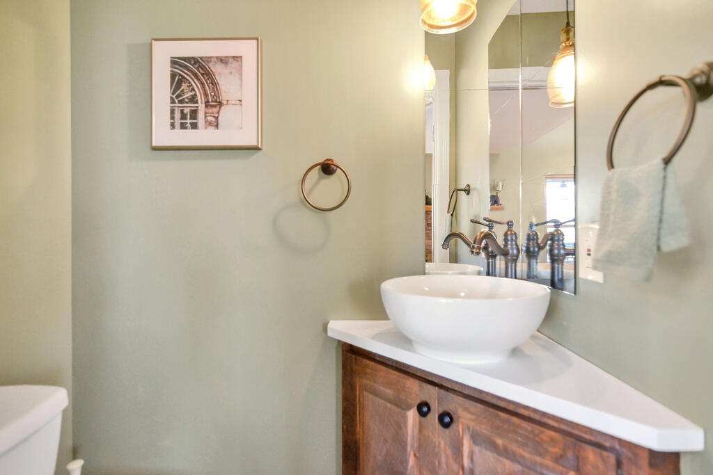 Bathroom vanity with a white vessel sink, rustic wood cabinet, and bronze faucet beneath a large mirror.