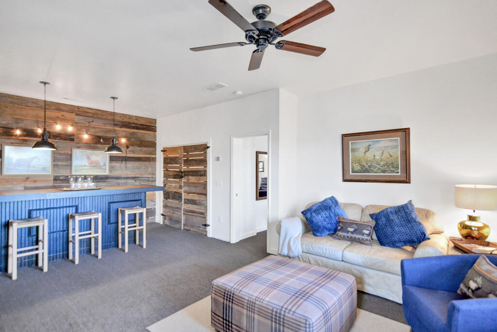 Furnished living room with blue bar, rustic wood accent wall, and ceiling fan.