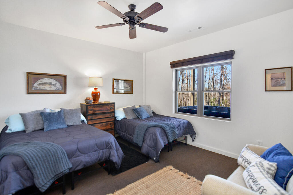 Bedroom with two gray-covered beds, a wooden chest, and a window overlooking trees.