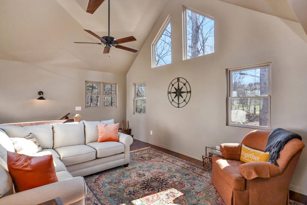 Vaulted living room with tall windows, a pale sofa, rust-colored armchair, and patterned rug.