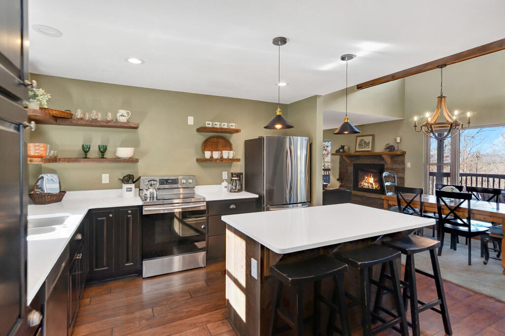 Kitchen with a large white island, dark cabinetry, and an open dining area beside a fireplace.