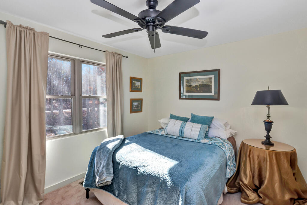 Bedroom with blue bedding, a large curtained window, and a dark ceiling fan.