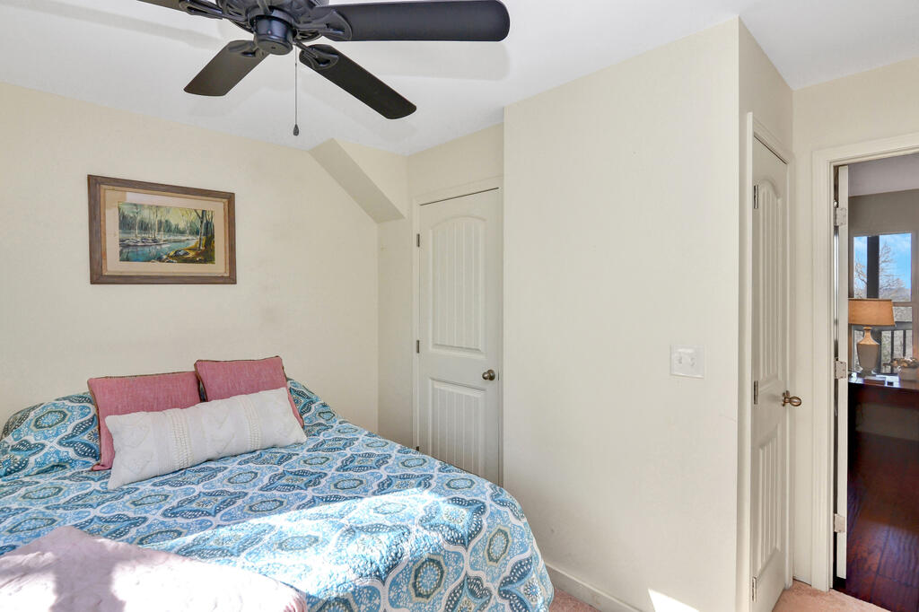 Bedroom with a blue patterned bedspread, pink pillows, and a ceiling fan.