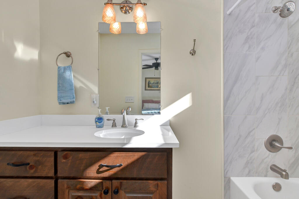 Bathroom vanity with dark wood drawers beside a marble-look tiled tub and shower.