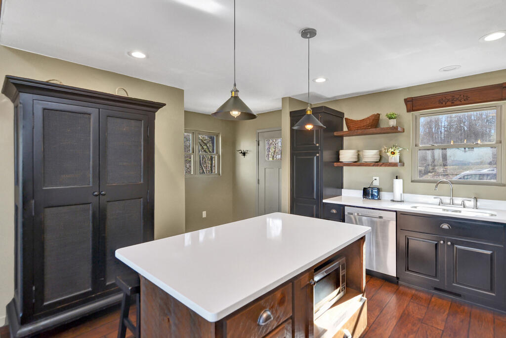 Kitchen with a large white island, dark cabinetry, and hardwood floors.