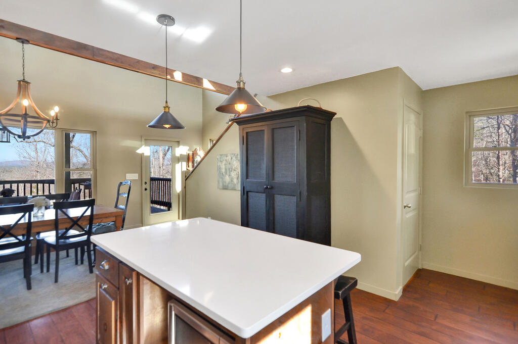 Kitchen with a large white island, dark cabinetry, and a dining area beside windows overlooking wooded hills.