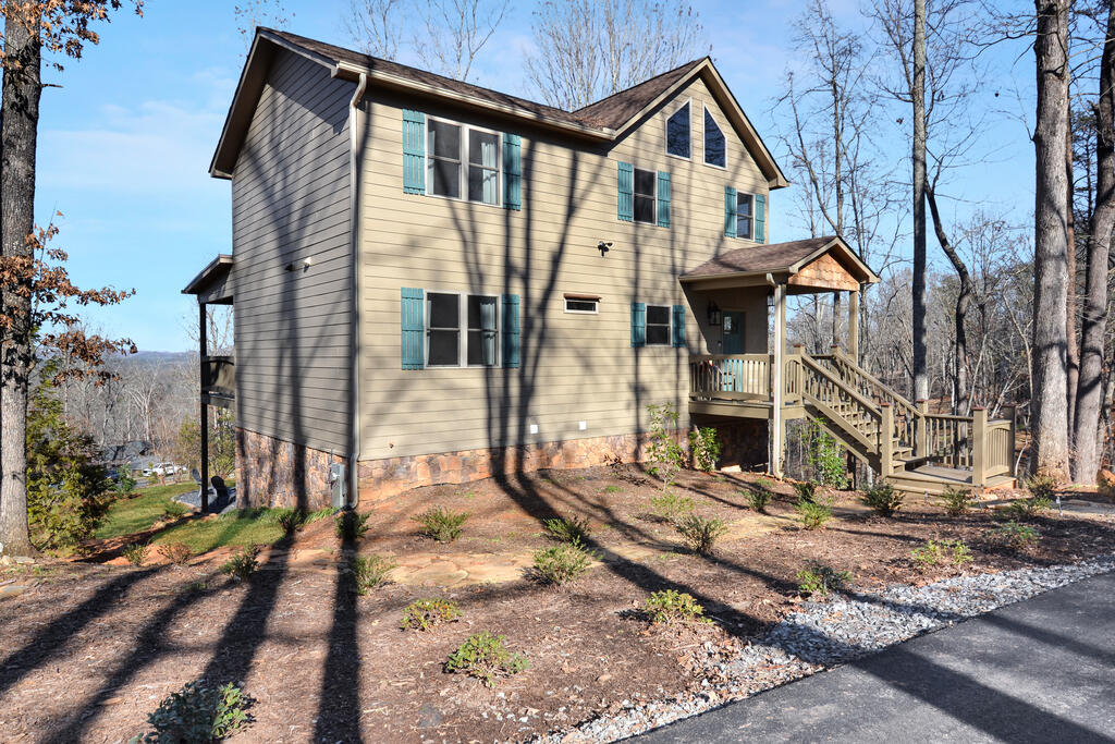 Two-story beige house with teal shutters, stone foundation, and a covered porch among leafless trees.