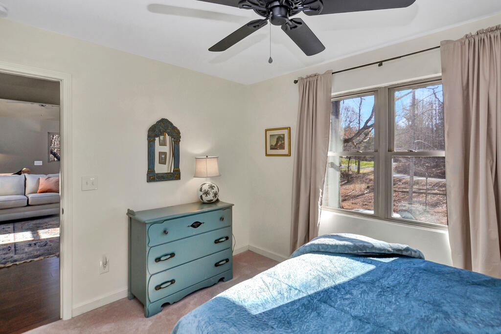 Bedroom with a blue quilted bed, turquoise dresser, and large windows overlooking trees.