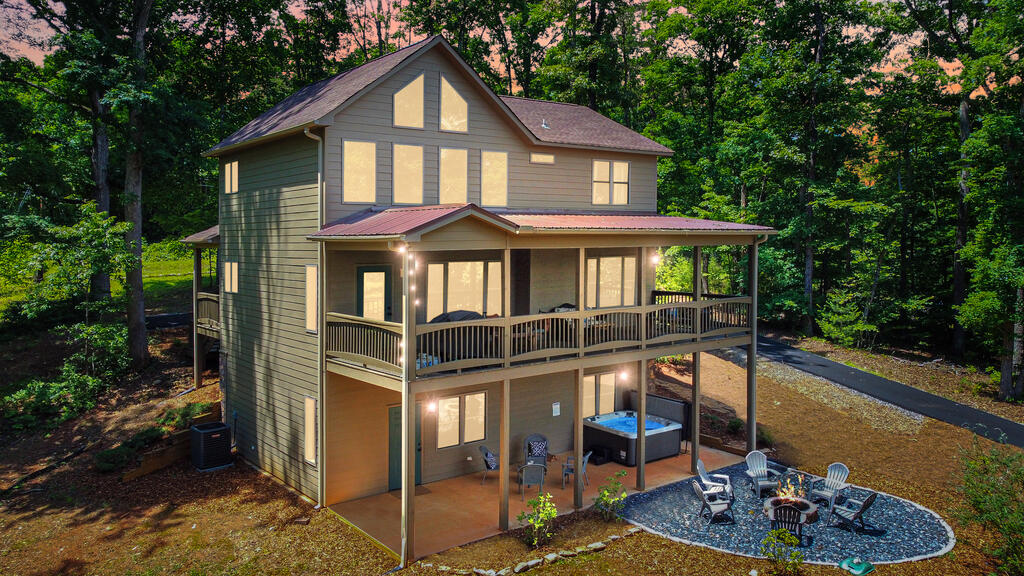 Two-story wooded home with a broad covered porch, hot tub, and fire pit seating area.