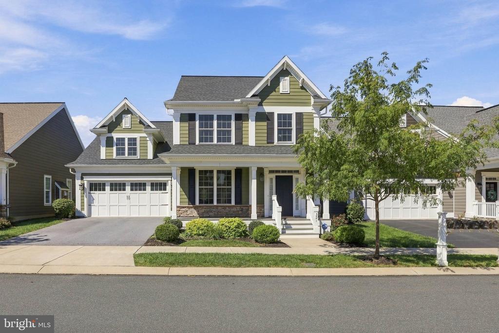 Green two-story house with white trim, a two-car garage, and a tree in front.