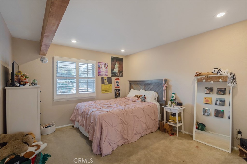 Bedroom with a pink quilted bed, shuttered window, exposed wooden beam, and full-length mirror.