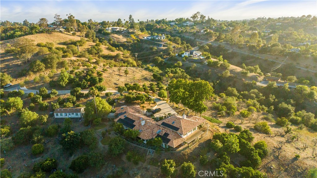 Aerial view of a tiled-roof home on dry, rolling hillside land with scattered trees.