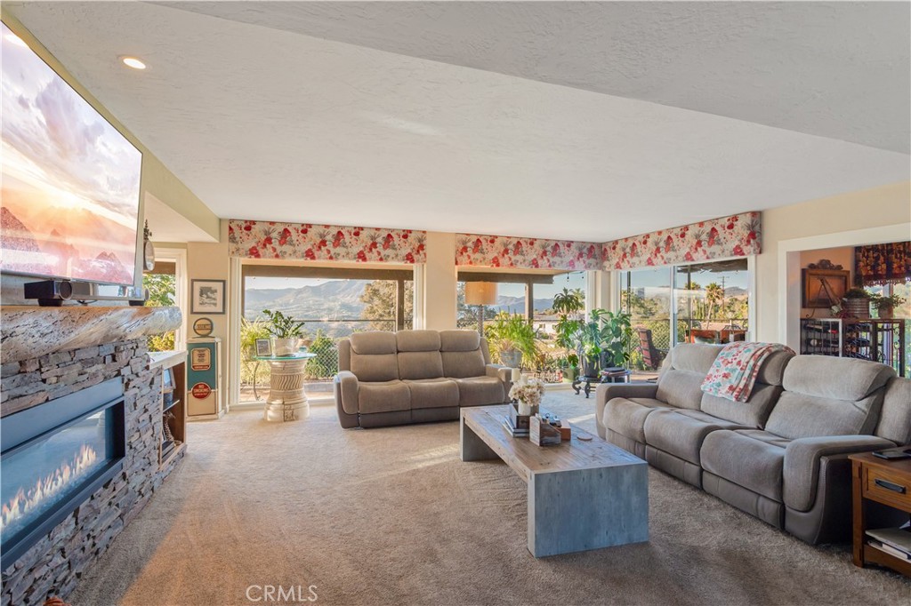 Living room with gray sofas, a stone fireplace, and large windows overlooking mountains.