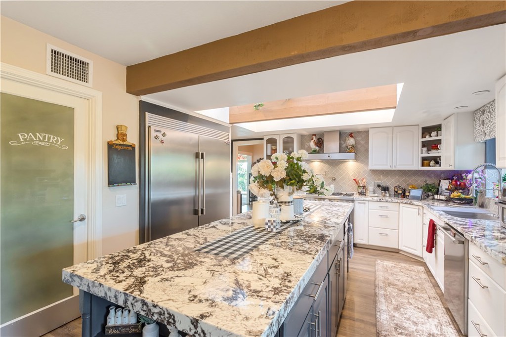 Kitchen with a large stone island, stainless steel refrigerator, white cabinets, and skylight.