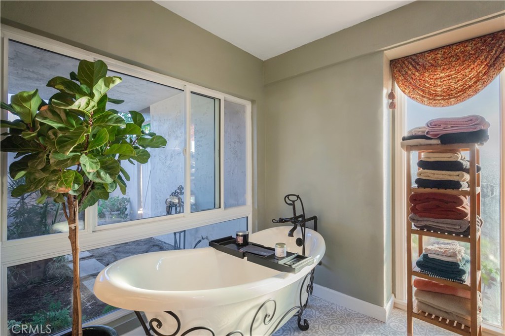 Bathroom with a freestanding white soaking tub beside large windows and a shelf of folded towels.