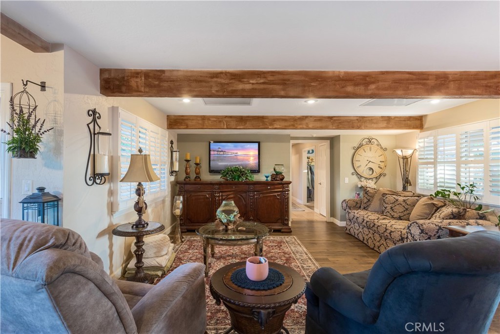 Furnished living room with exposed wood beams, plantation shutters, and a patterned area rug.