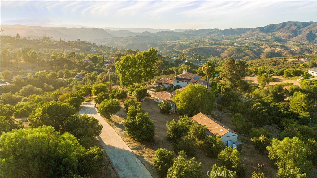 Aerial view of a hillside property with a long driveway, mature trees, and distant mountains.