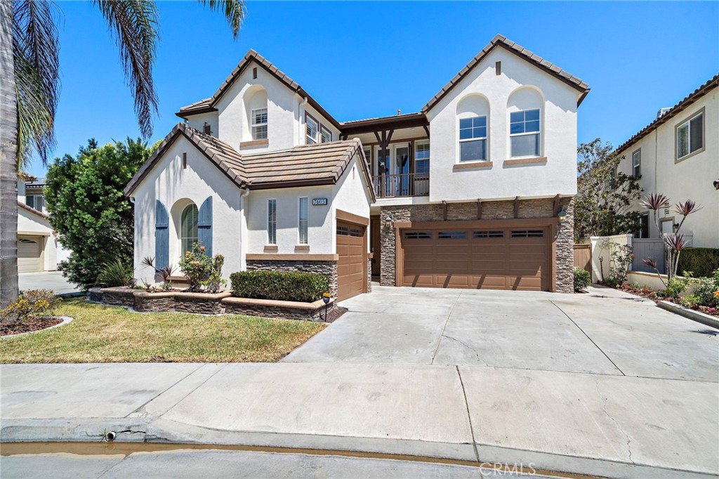 Two-story white stucco home with a brown tile roof, stone-accented double garage, and wide driveway.