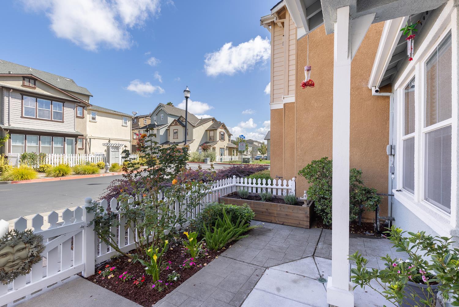 Landscaped front patio with gray pavers, raised flower beds, and a white picket fence.