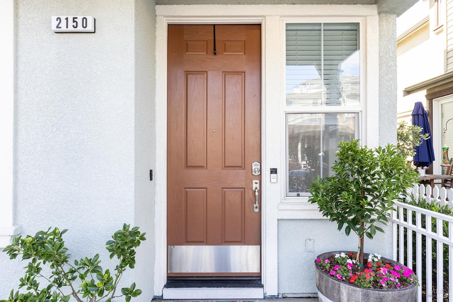 Home entry with a brown paneled door, window, and flower-filled planter.