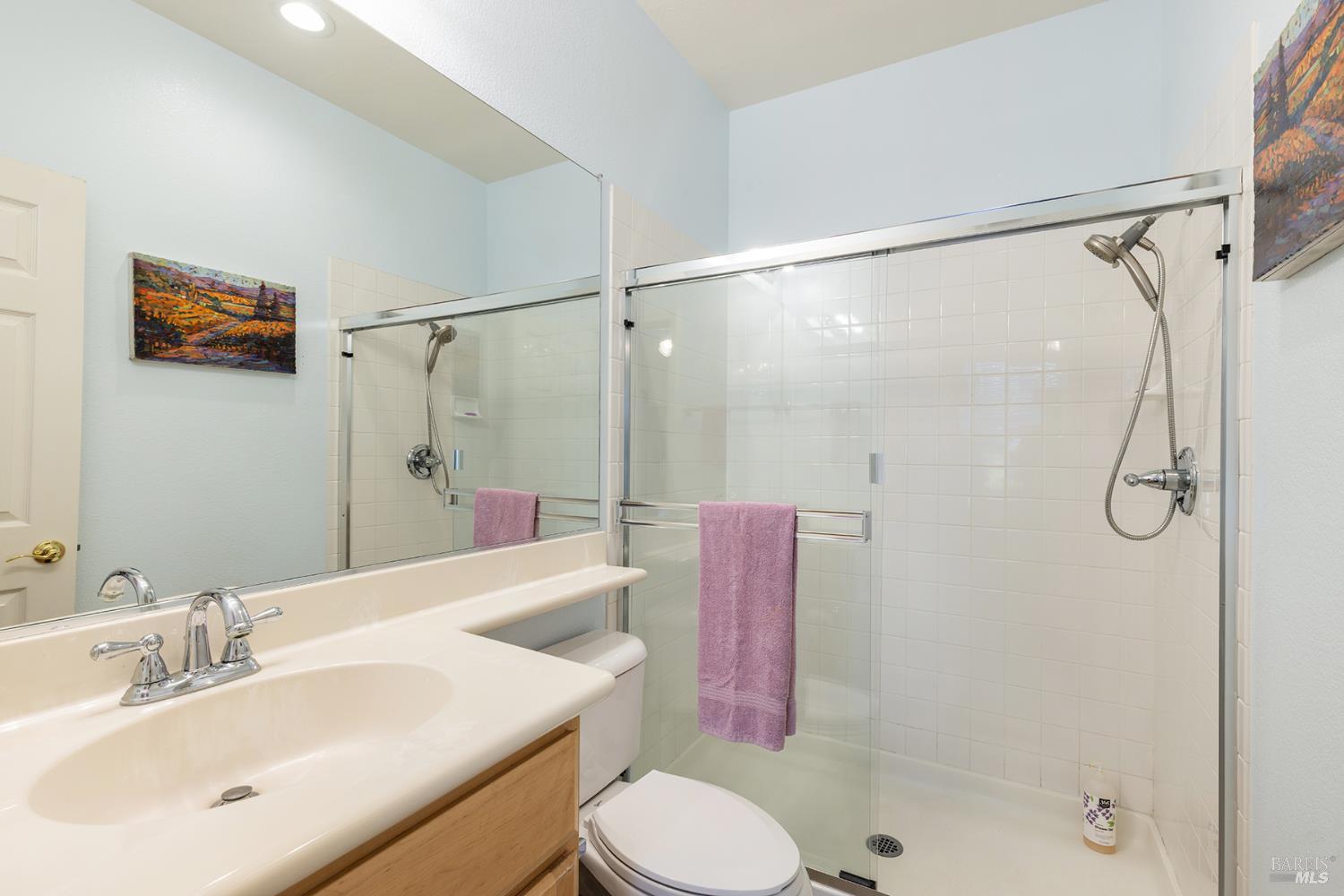Bathroom with a glass-enclosed white-tiled shower, wood vanity, and purple towel.
