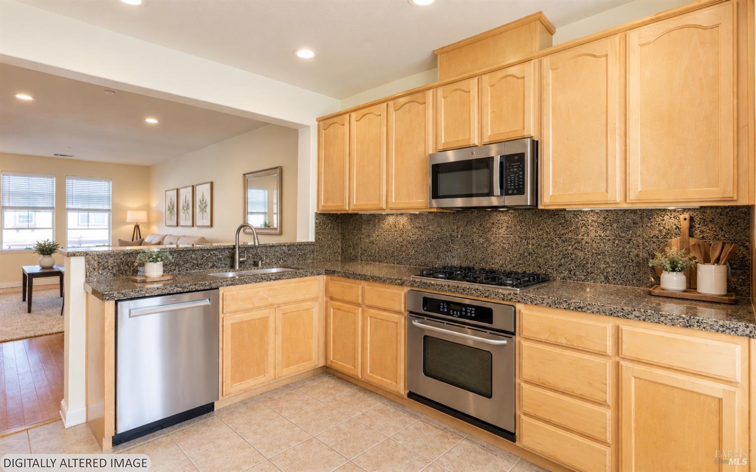 Kitchen with light maple cabinets, patterned stone counters, and stainless steel appliances.