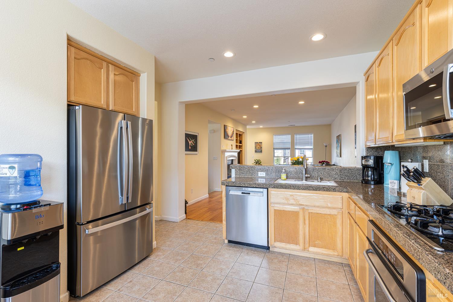 Kitchen with light wood cabinets, granite counters, stainless steel appliances, and a central sink.