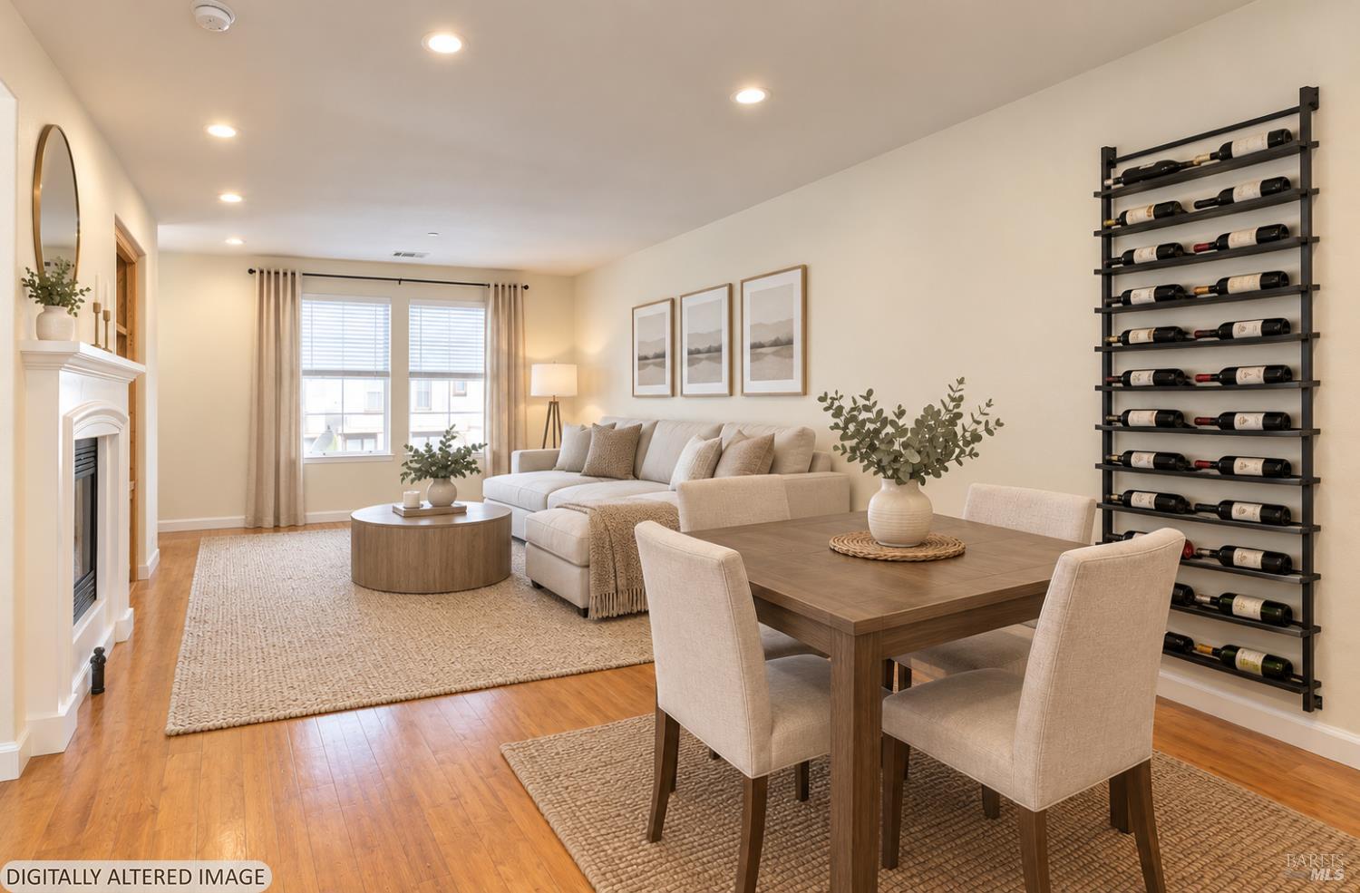 Staged living and dining room with a cream sectional, white fireplace, hardwood floors, and wall-mounted wine rack.