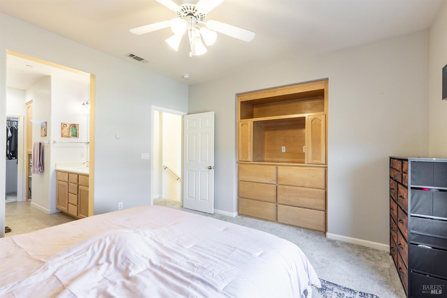 Bedroom with a built-in wooden dresser and shelving beside an open bathroom doorway.