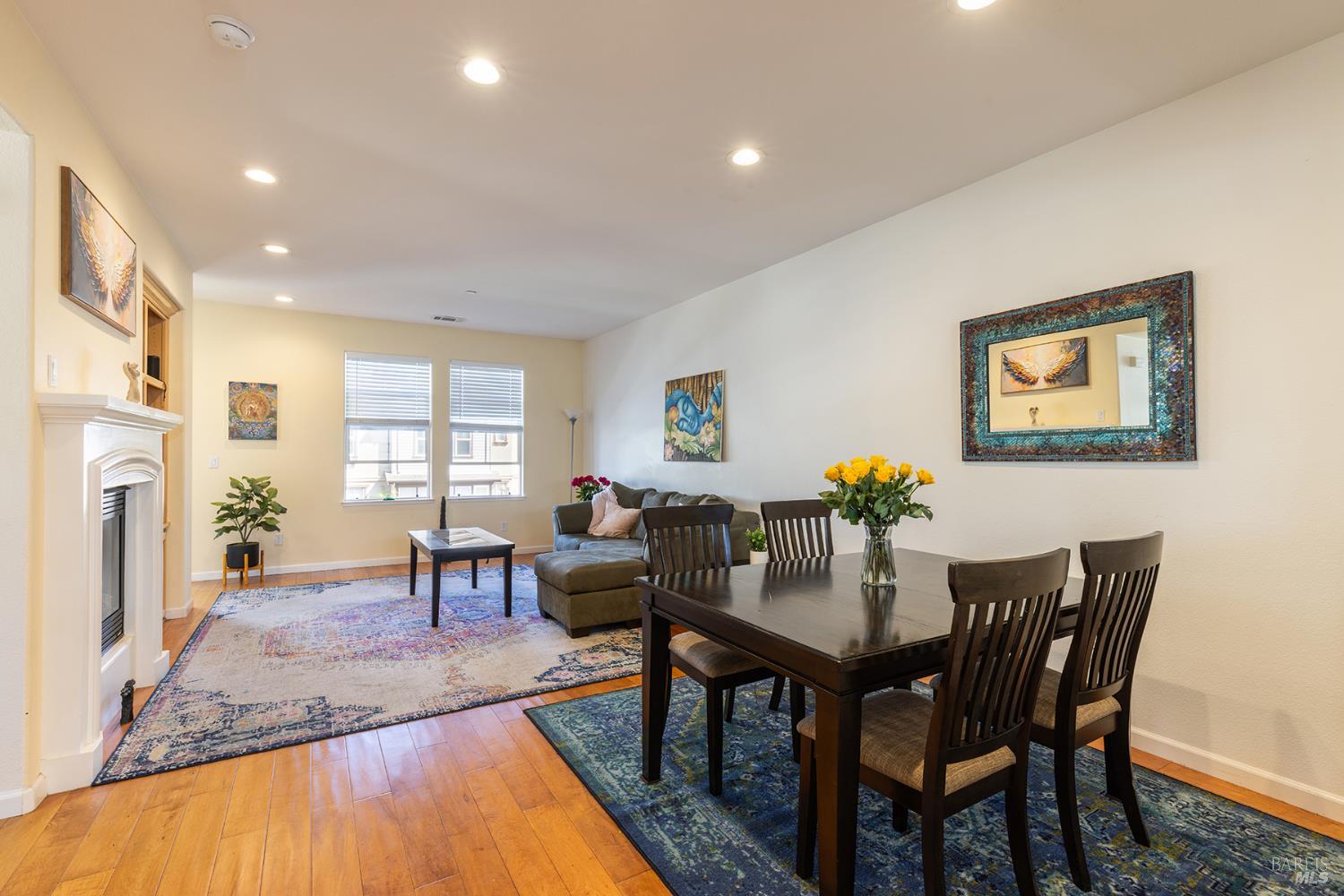 Open-plan living and dining room with a white fireplace, gray sectional, and dark wood dining table.