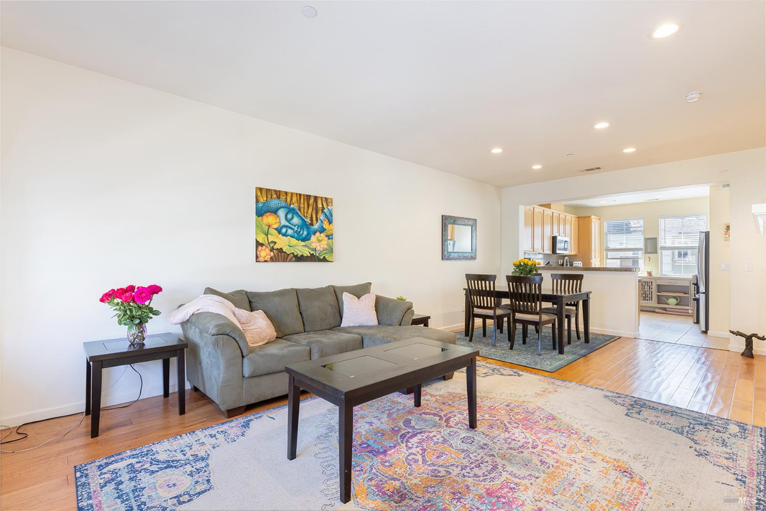 Open-plan living and dining area with a gray sofa, colorful rugs, and kitchen beyond.