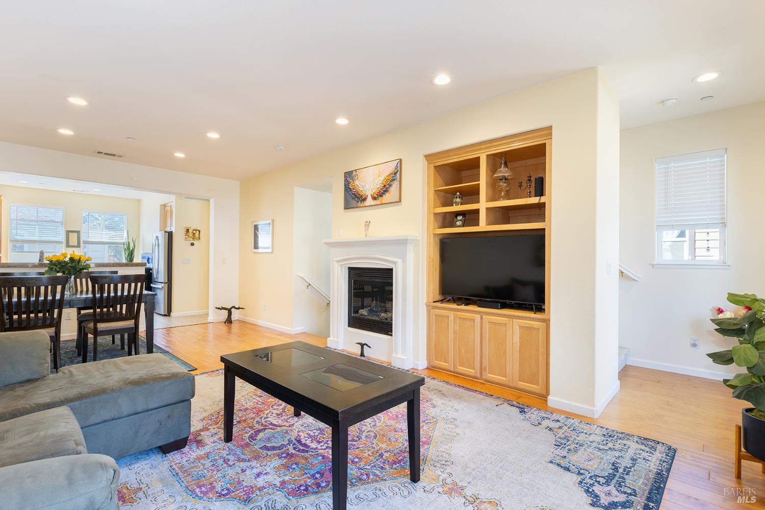 Living room with a fireplace and built-in wooden entertainment center, opening to the dining area and kitchen.