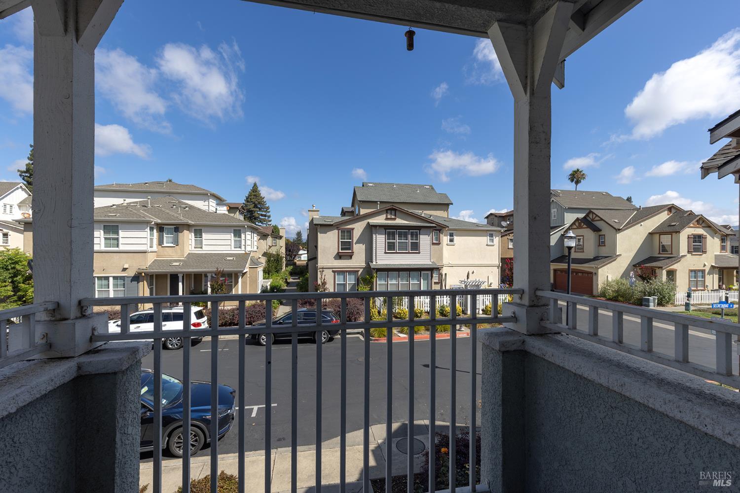 Covered balcony overlooks nearby homes and a residential street with parked cars.