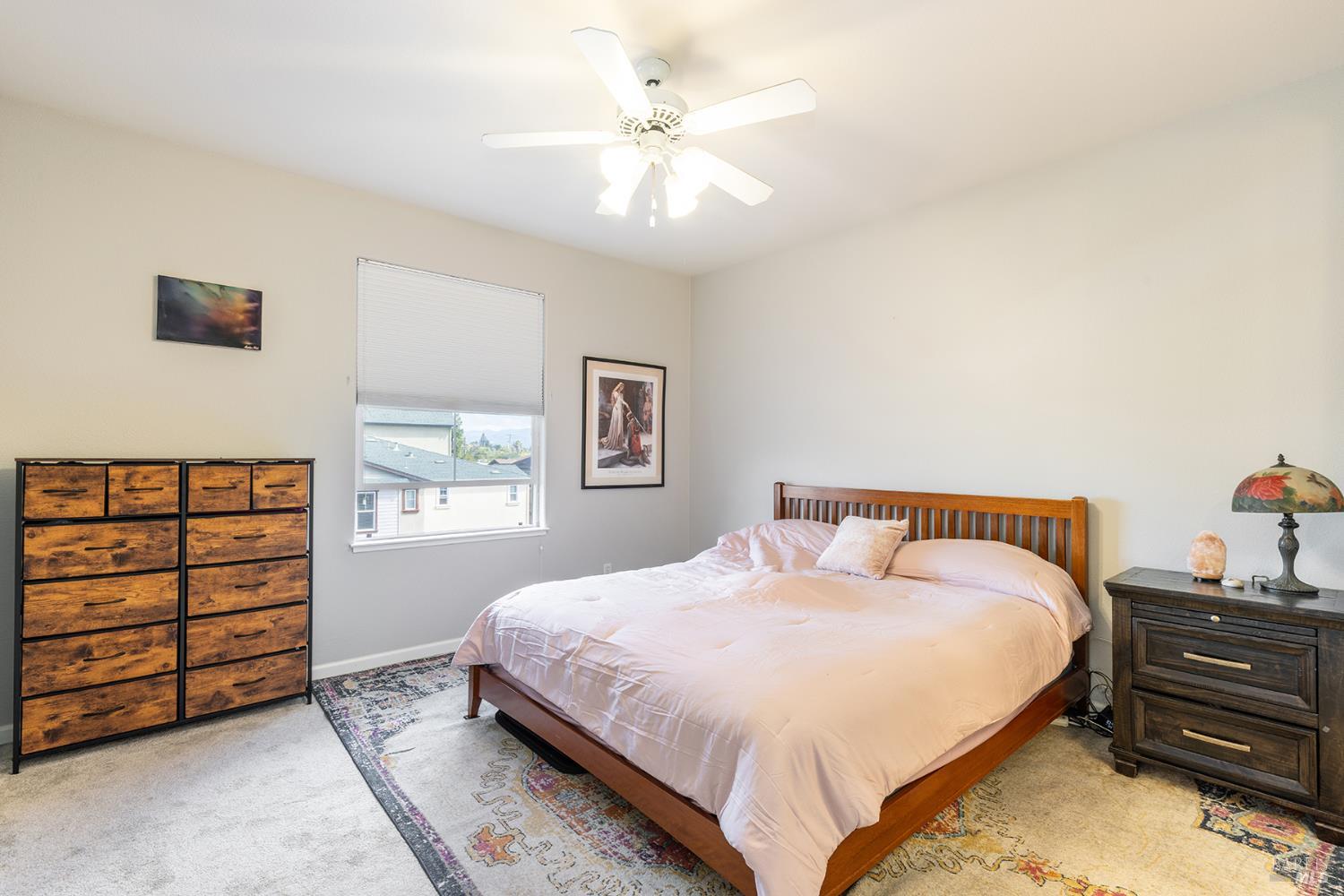 Bedroom with a wooden bed, pale pink bedding, matching dressers, patterned rug, and ceiling fan.
