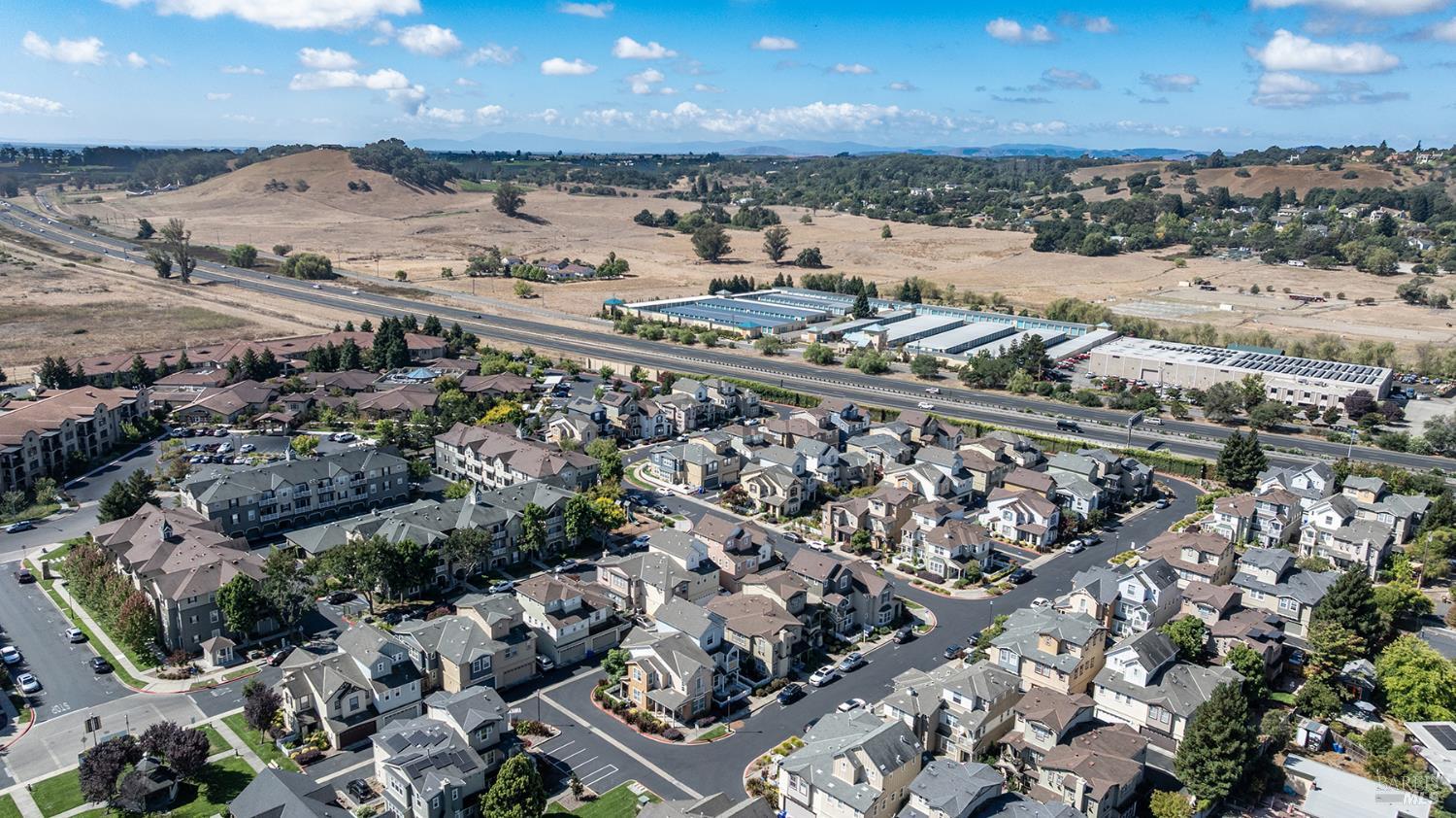 Aerial view of a residential neighborhood, with a highway and dry rolling hills in the distance.