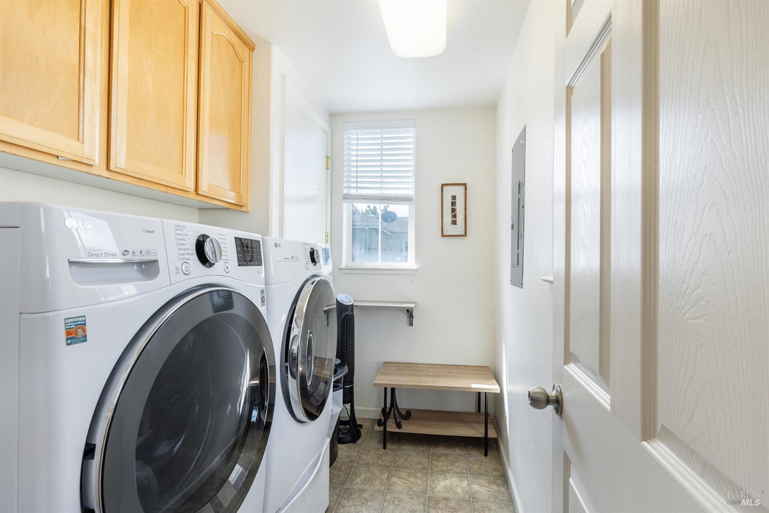 Laundry room with front-loading washer and dryer beneath wood cabinets and a window at the far end.