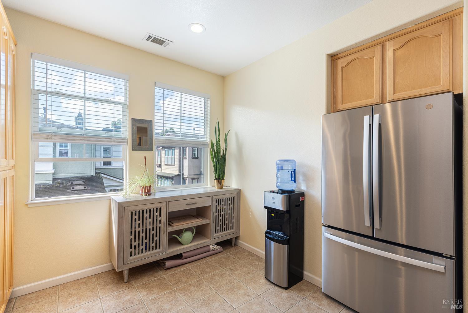 Kitchen with a stainless steel refrigerator, wood cabinets, and windows overlooking neighboring buildings.