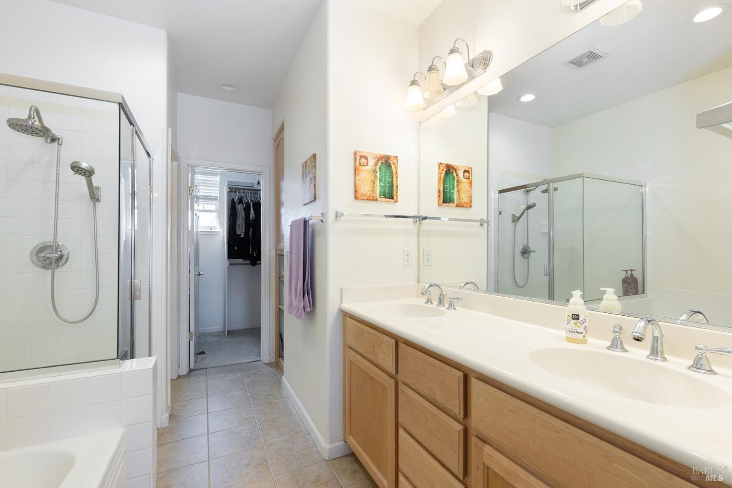Bathroom with a long double vanity, wood cabinets, large mirror, and glass-enclosed shower.