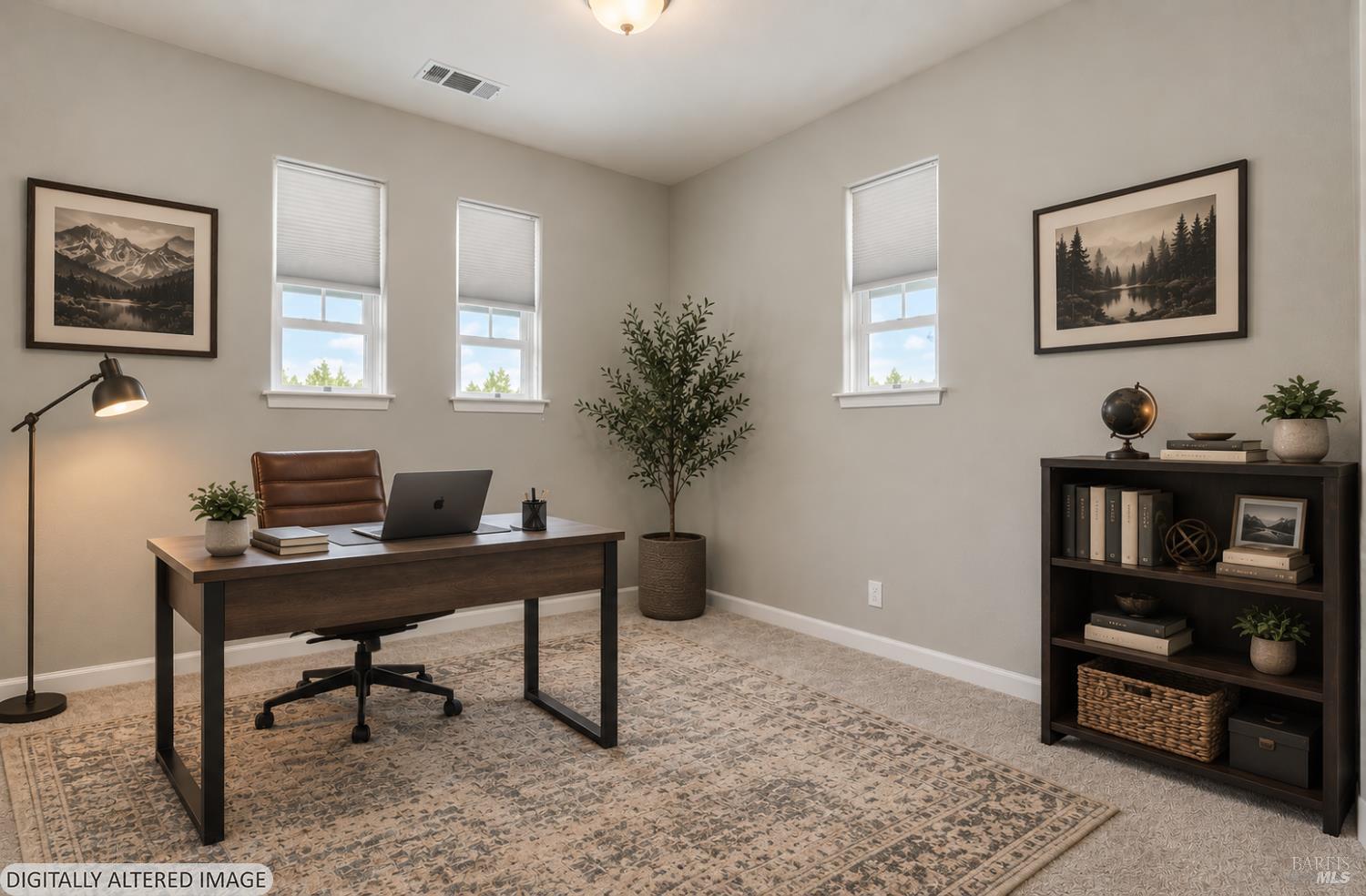 Furnished home office with a dark desk, laptop, bookcase, and three bright windows.