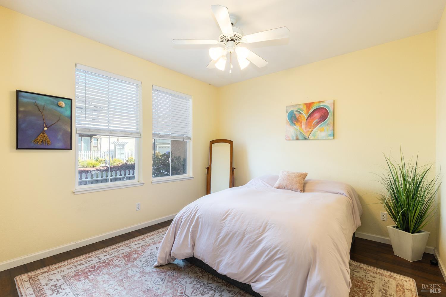 Bedroom with a white bed, yellow walls, two windows, and a ceiling fan.