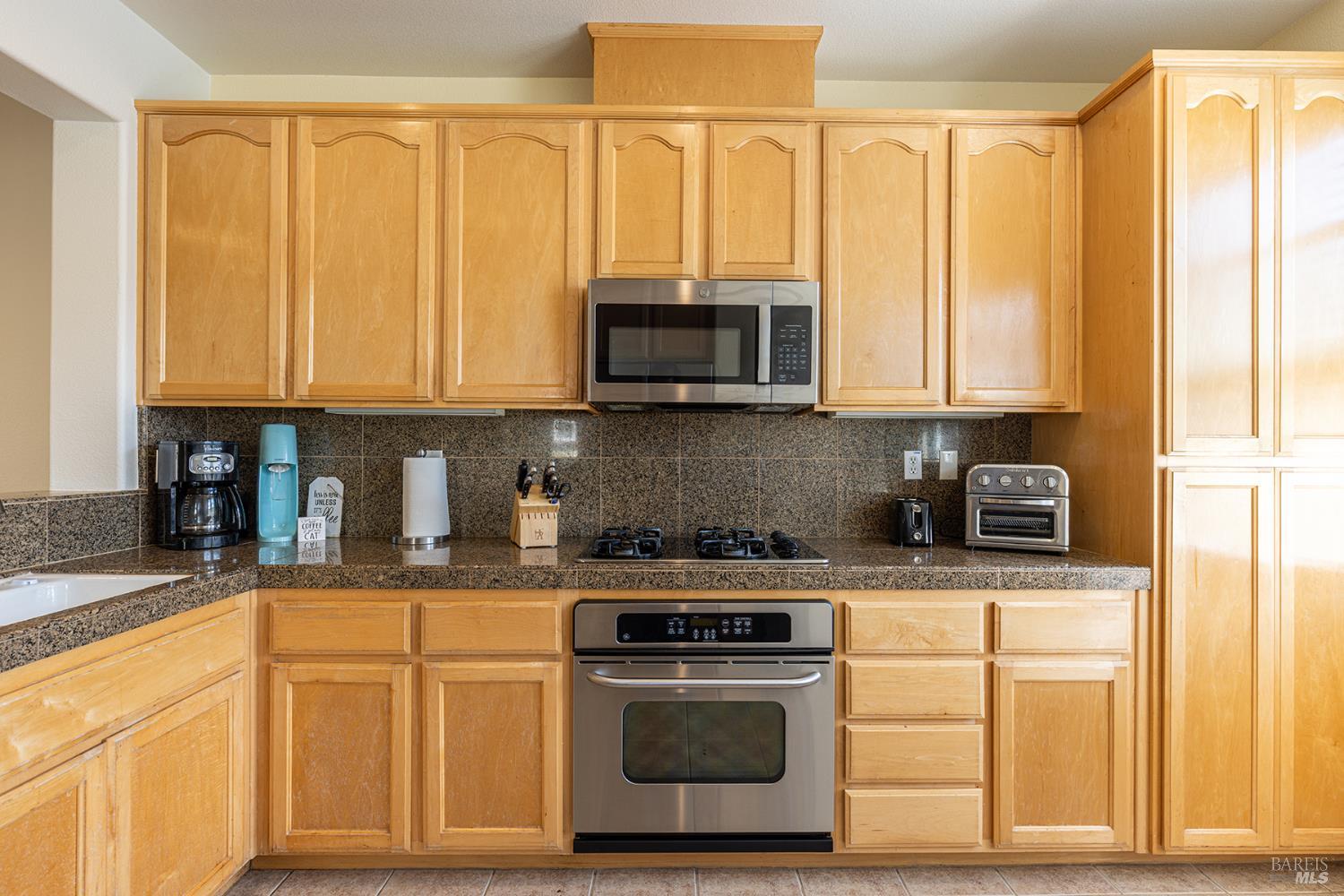 Kitchen with honey-colored cabinets, granite counters, stainless steel appliances, and a gas cooktop.