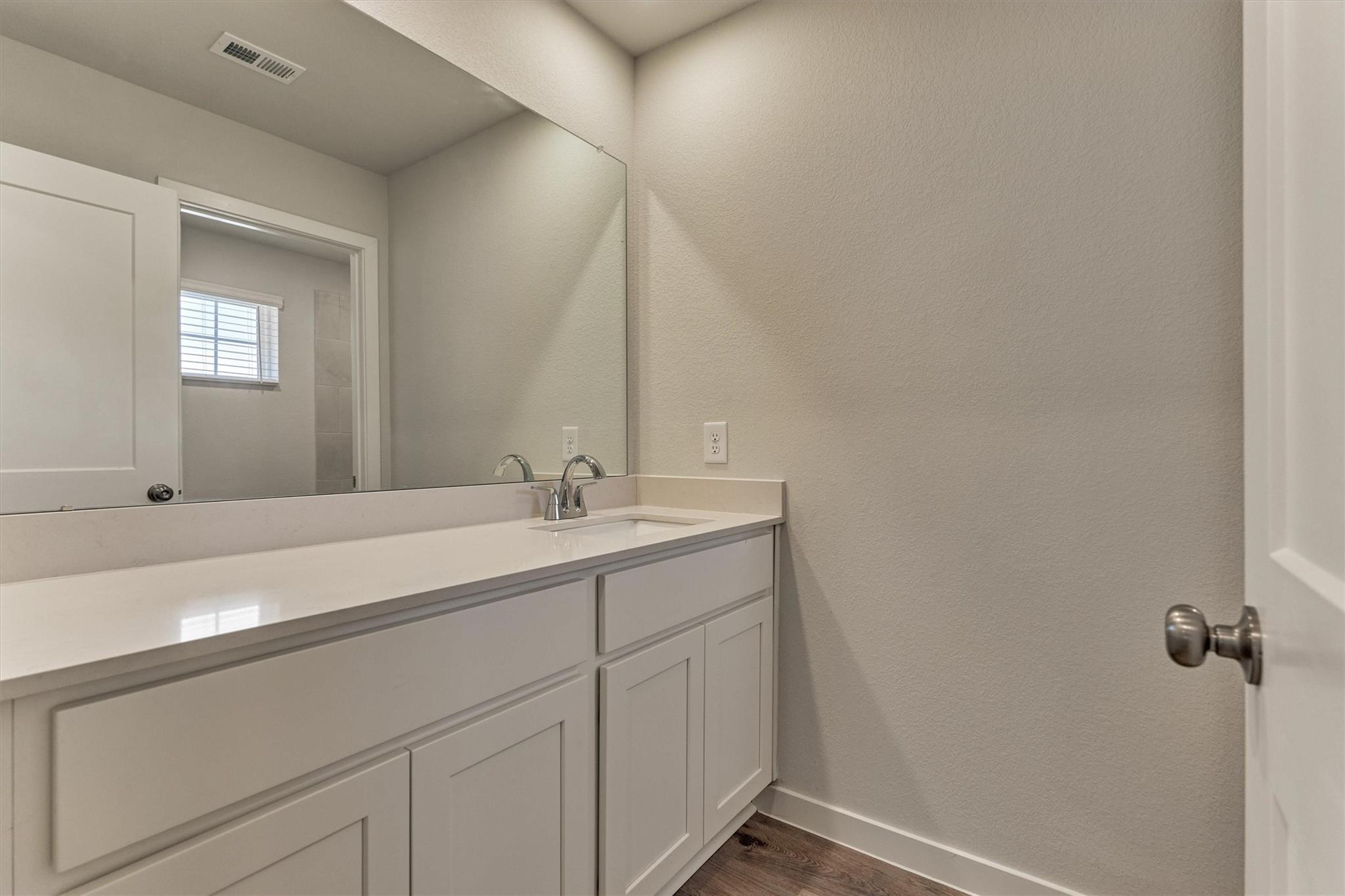 Bathroom vanity with a large mirror, white cabinetry, and a single sink.
