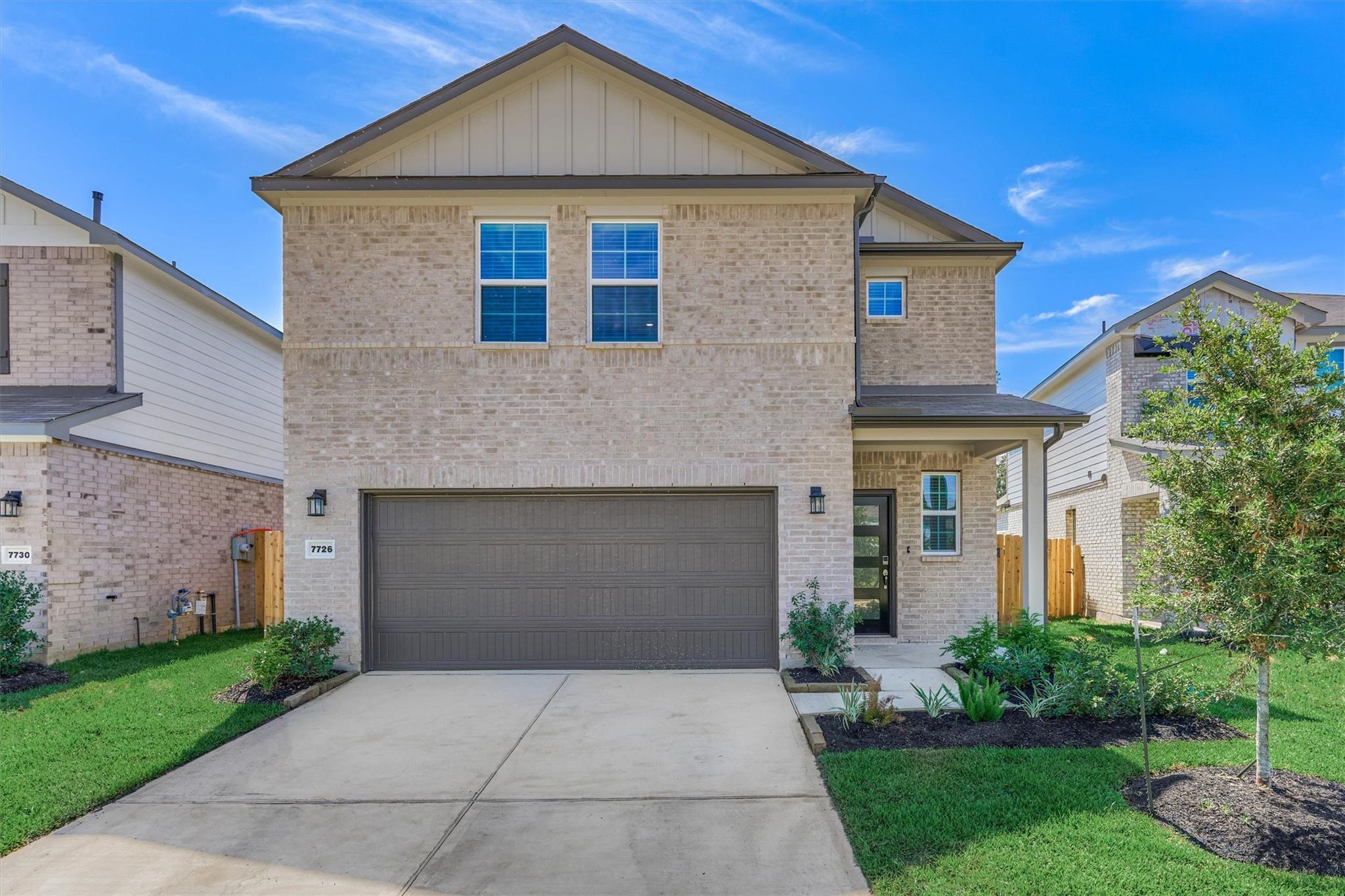 Two-story brick house with a wide double garage, driveway, and landscaped front lawn.