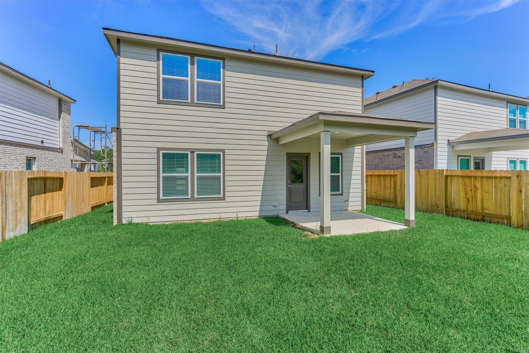 Two-story home with a covered rear patio, fenced yard, and broad green lawn.