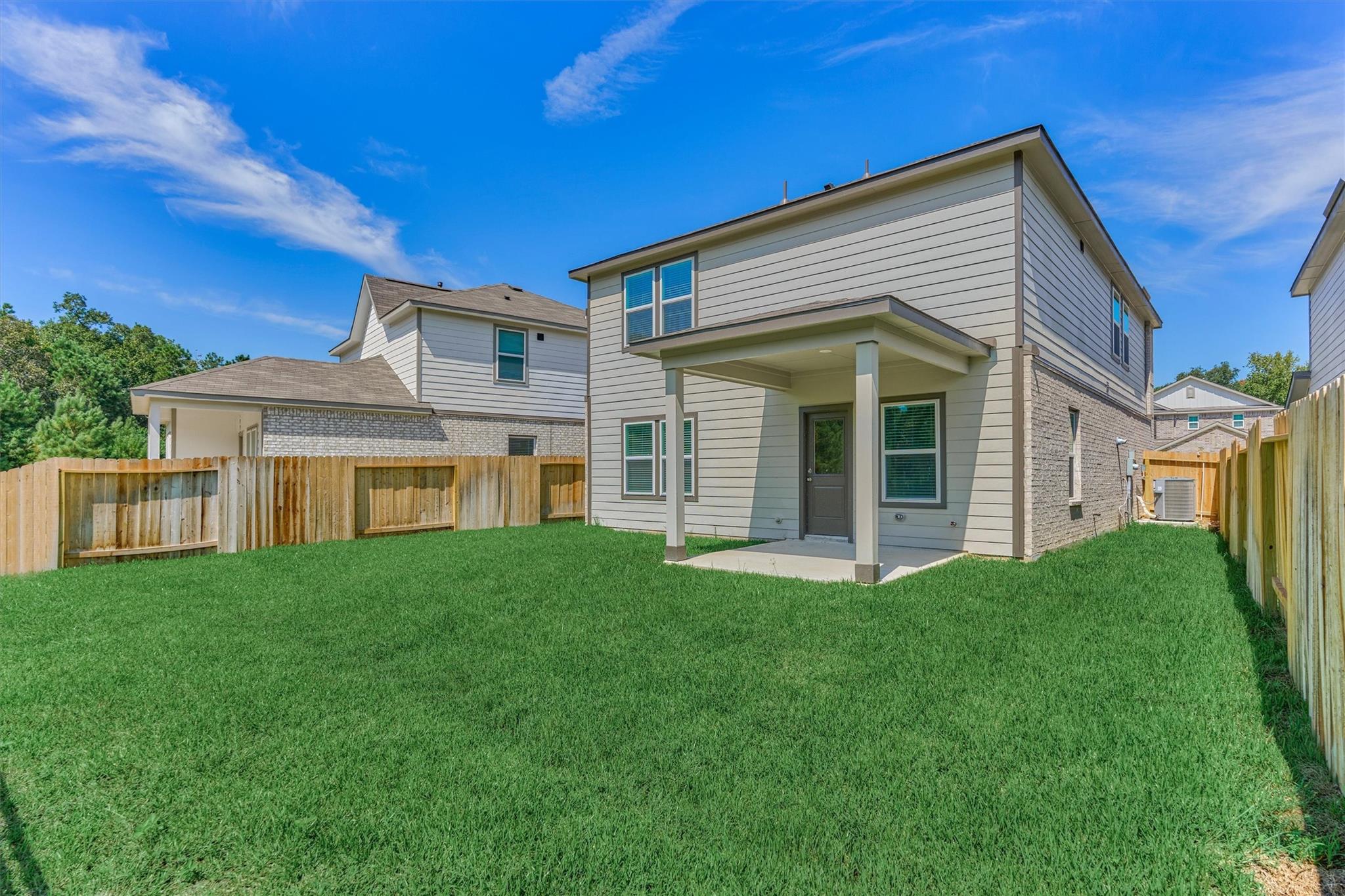 Two-story house with a covered back patio, fenced yard, and broad green lawn.