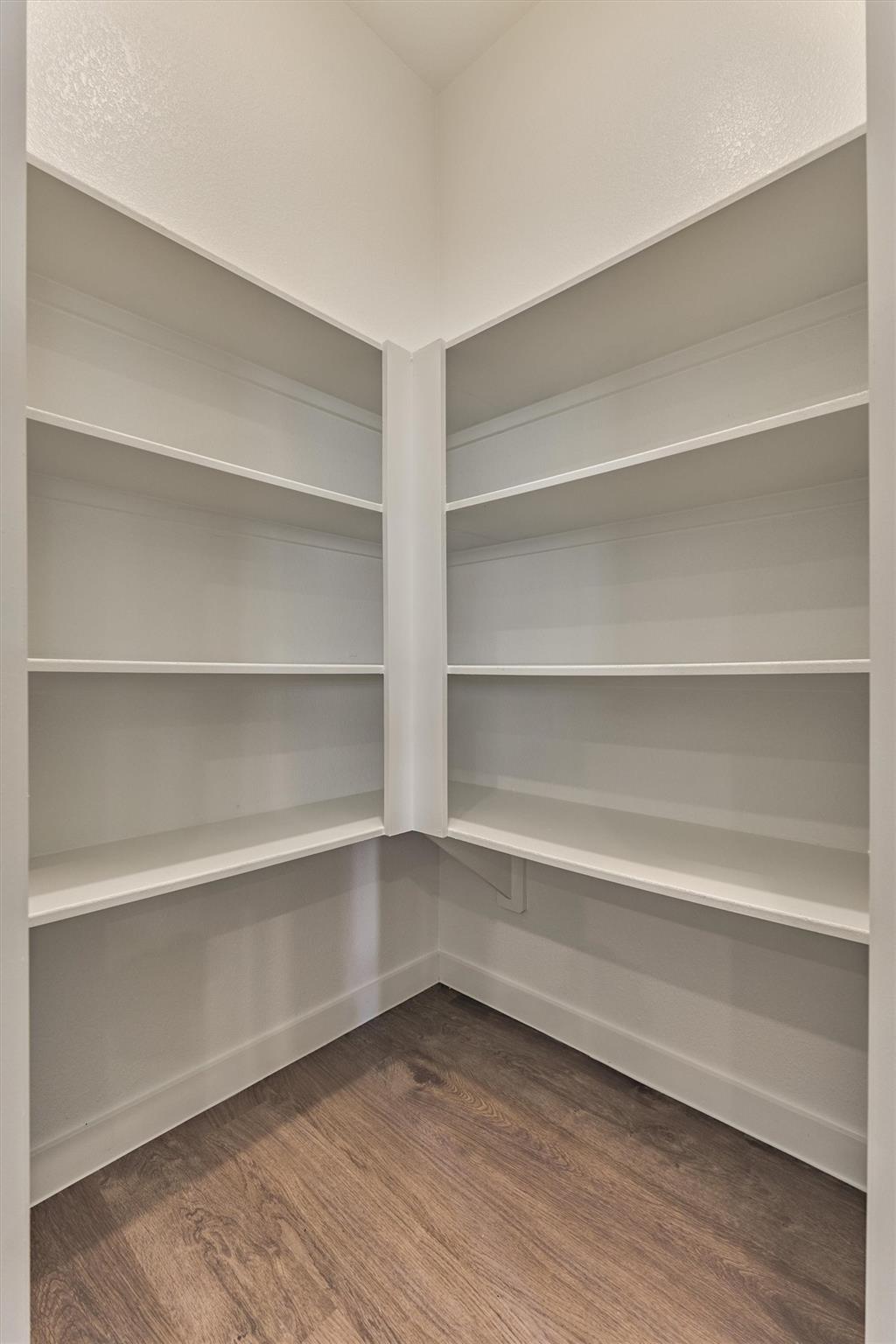 Walk-in closet with wraparound white shelving and dark wood-look flooring
