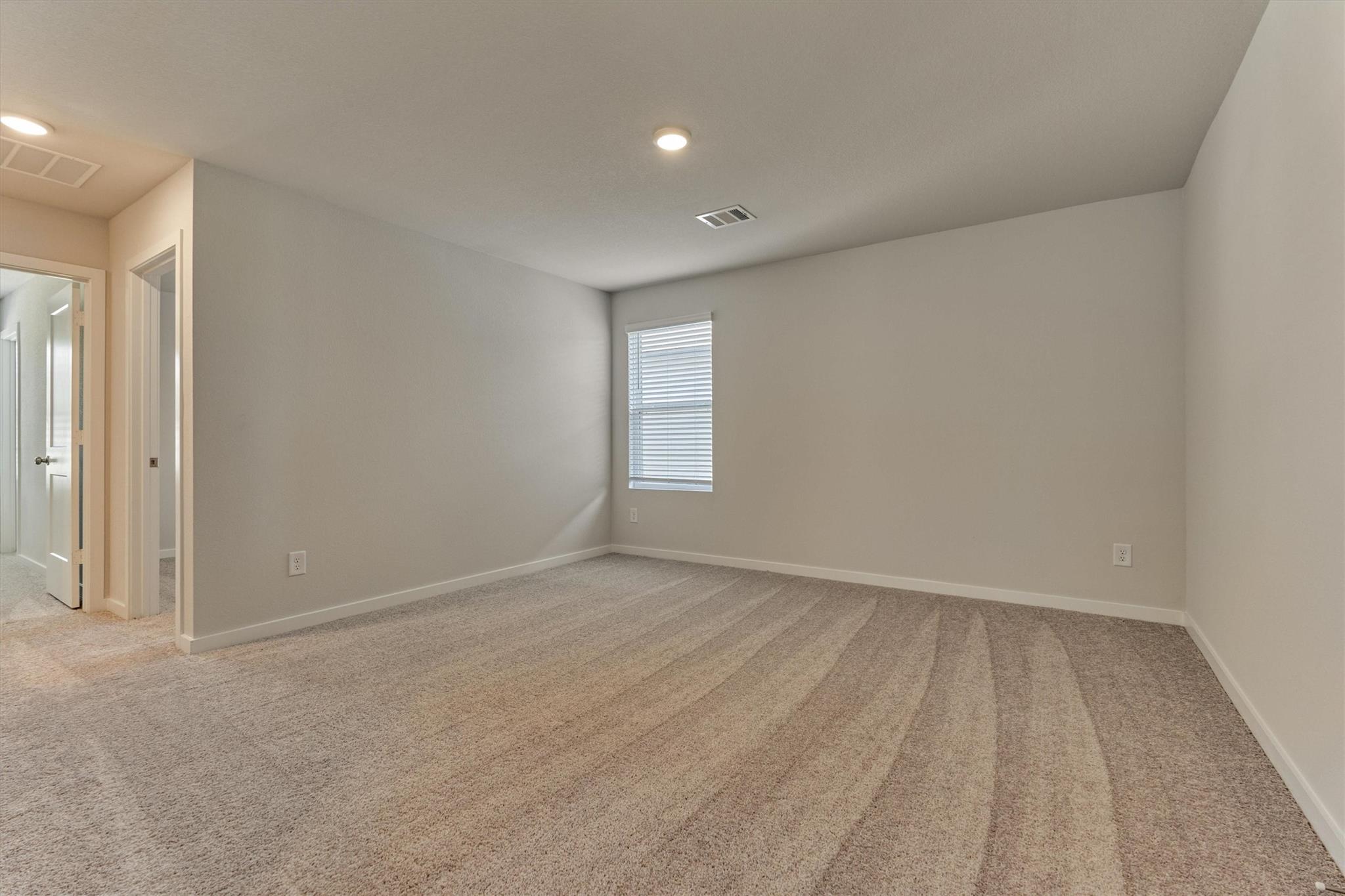 Empty bedroom with beige carpet and a window with blinds.