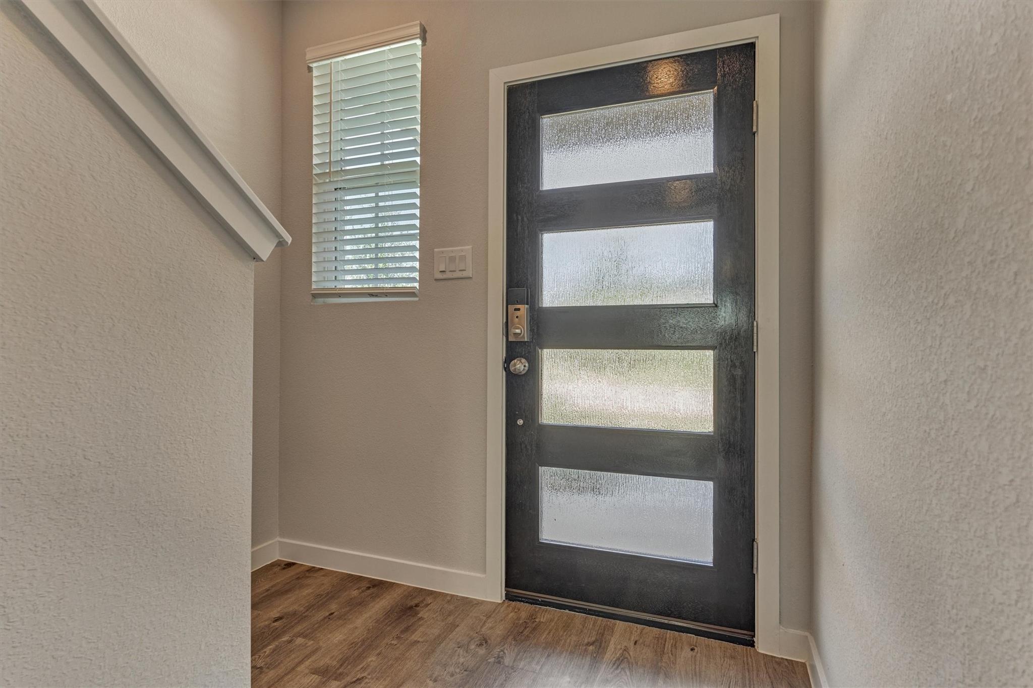 Entryway with a dark front door featuring four frosted glass panels beside a narrow window with blinds.