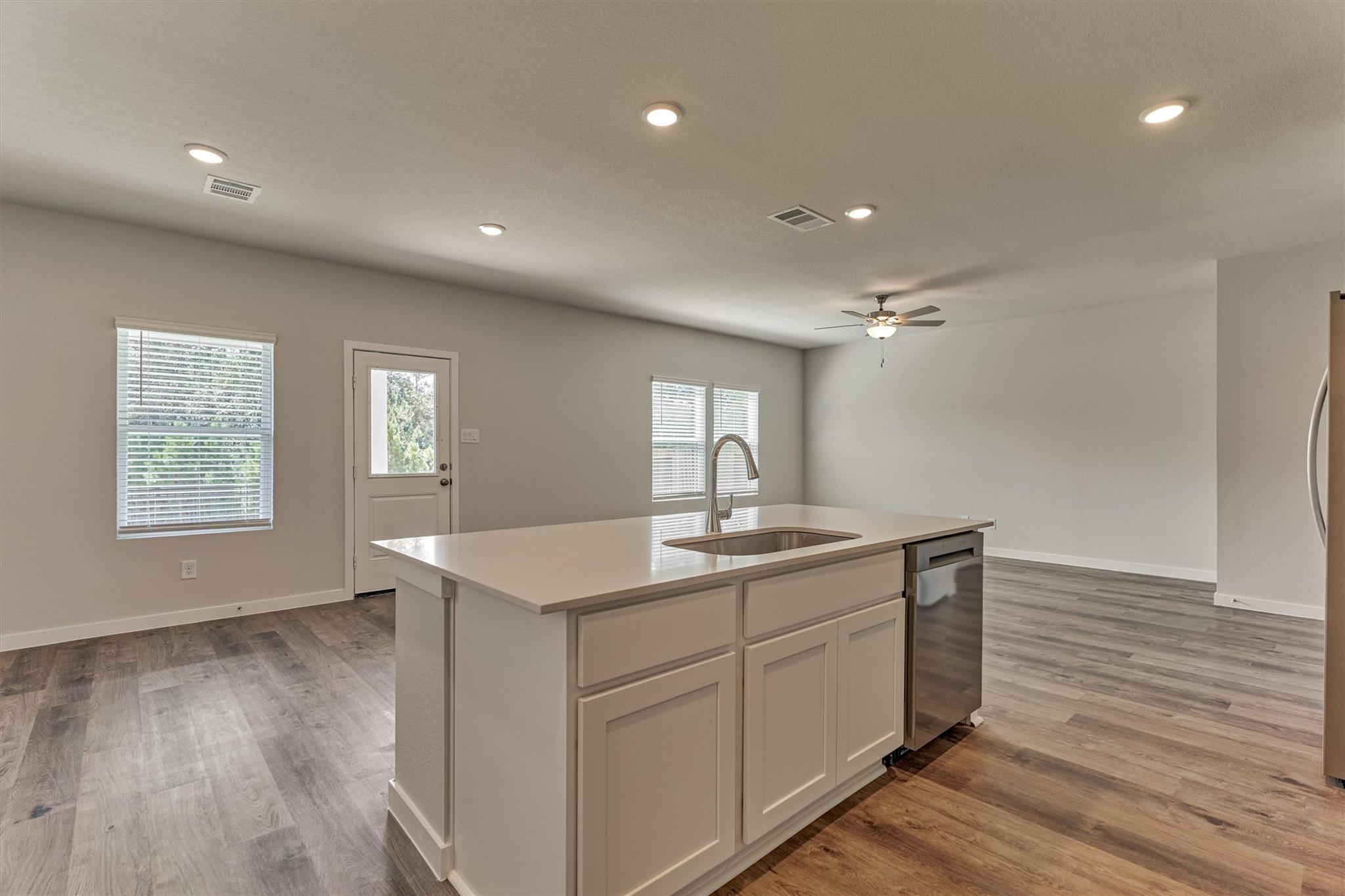 Vacant kitchen with a large white island, stainless steel dishwasher, and gray wood-look flooring.